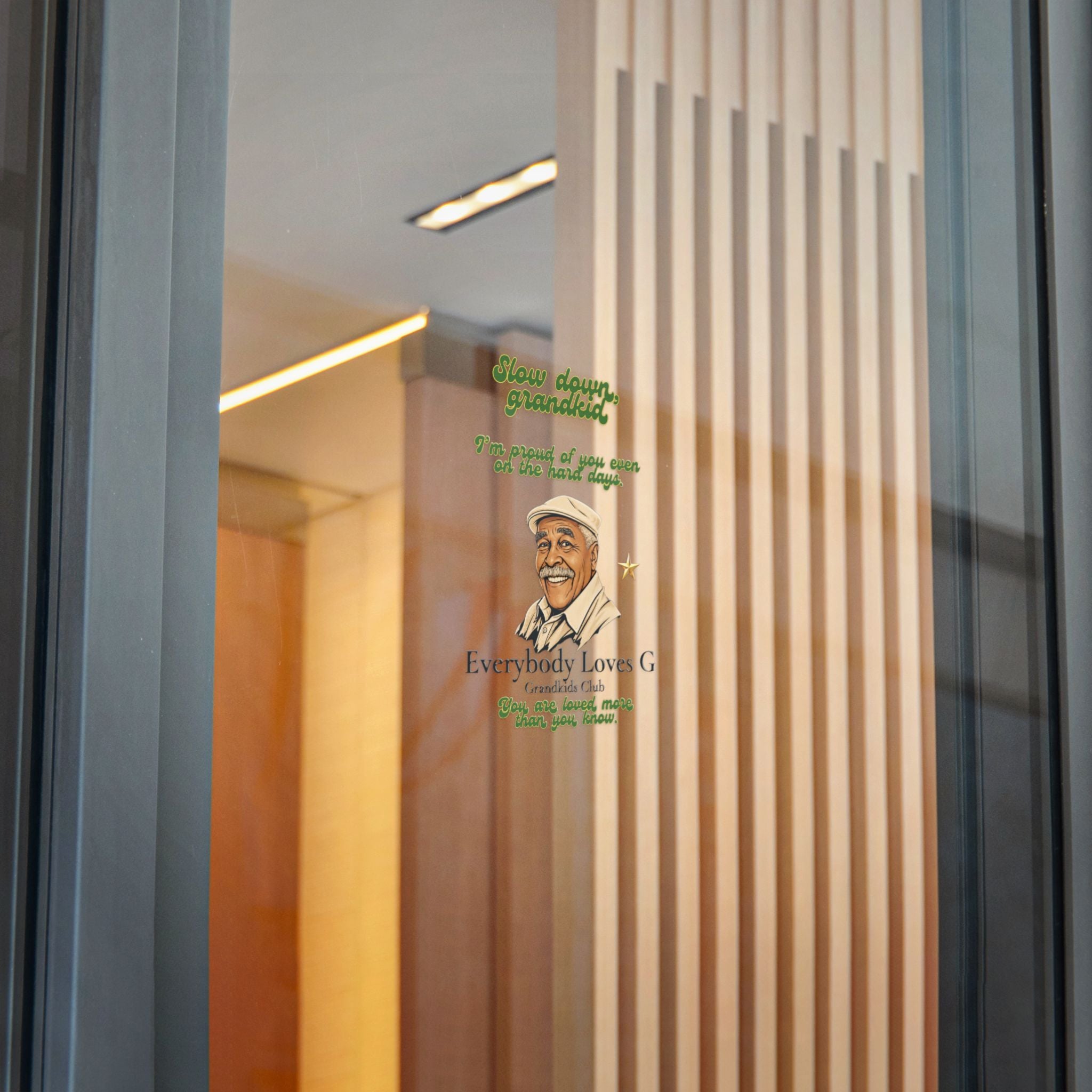Everybody Loves G affirmation sticker featuring Grandpa G illustration and message applied to a glass door in a modern indoor setting